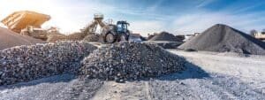 a modern construction site in fredericksburg features cutting-edge gravel-spreading machinery in action, surrounded by large piles of gravel and project managers reviewing blueprints on sleek tablets, all under a bright, clear sky.